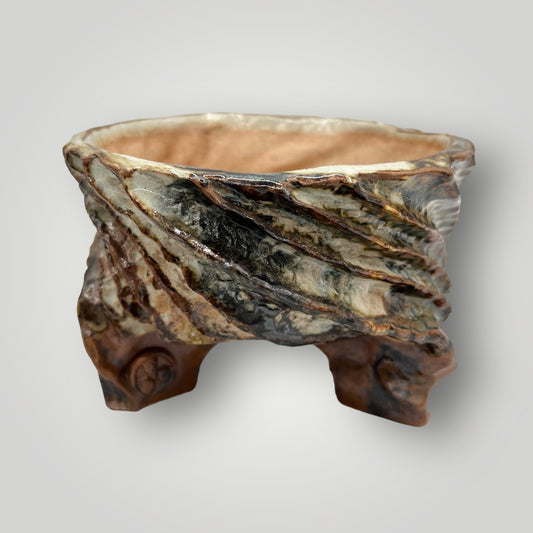 This unique pot features a rustic and organic design, reminiscent of natural elements. The body of the pot is irregularly shaped with a wide opening at the top. The exterior showcases a textured pattern with striations in shades of brown, cream, and touches of black, giving it an earthy and rugged appearance. This pot could serve as an eye-catching decorative piece for your plants.&nbsp;